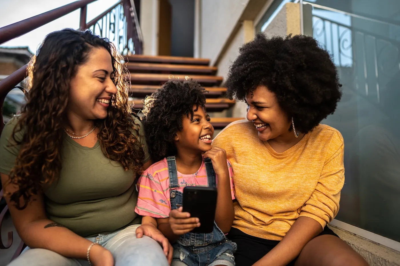 A young girl having fun with her mothers using mobile phone sitting on house steps outdoors