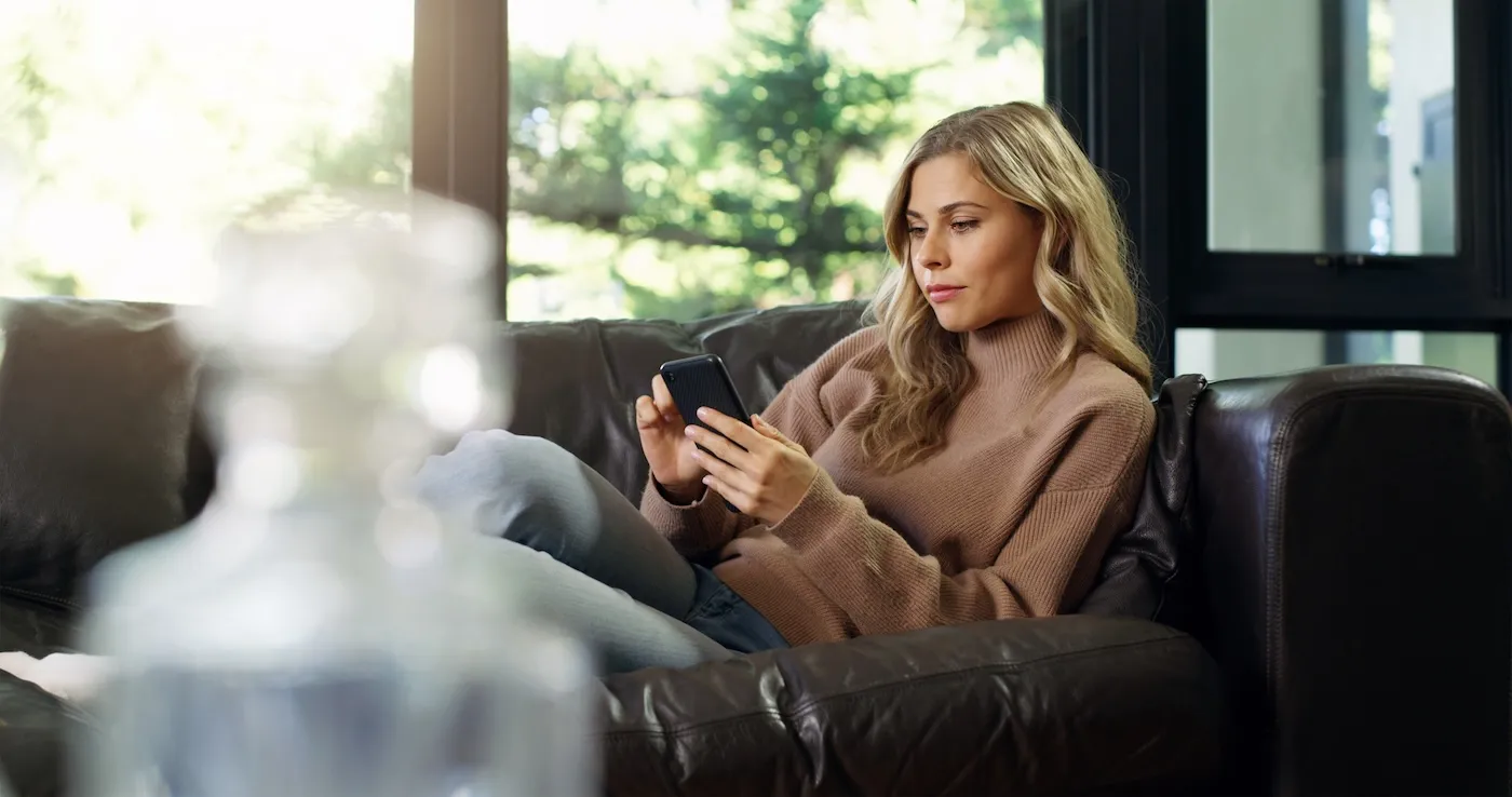 woman on phone on home living room sofa.