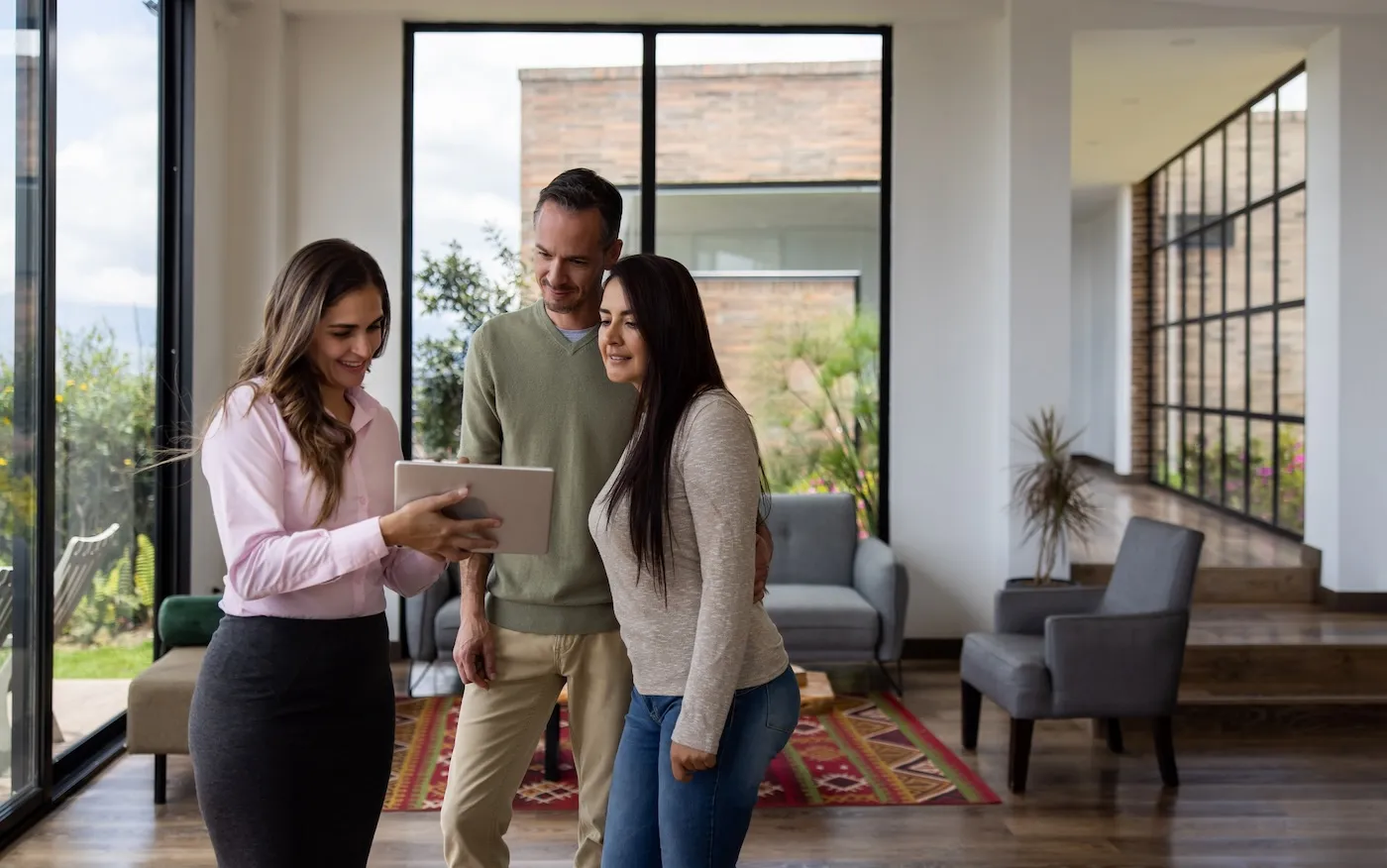 A landlord showing a house for sale to a couple and looking at the details on a tablet.