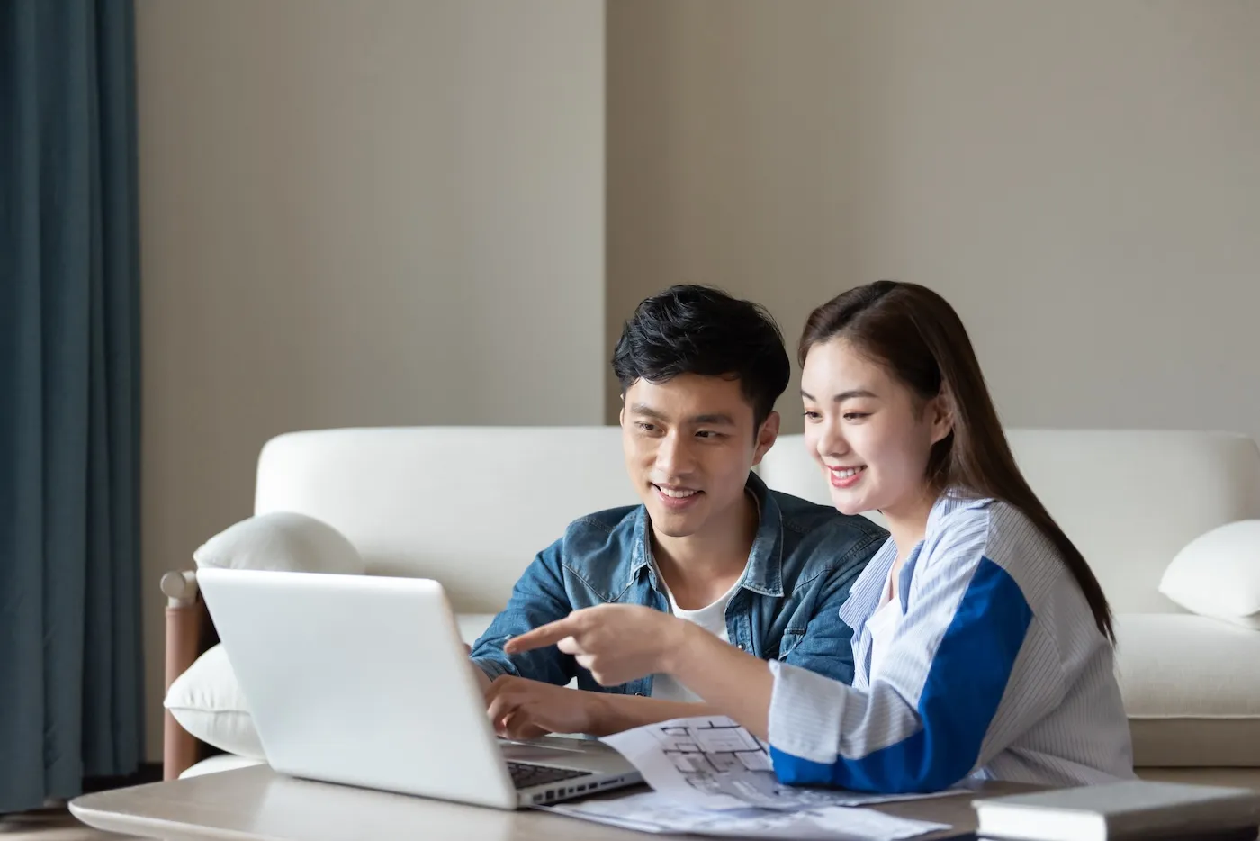 A young couple is sitting on a carpet using a computer.