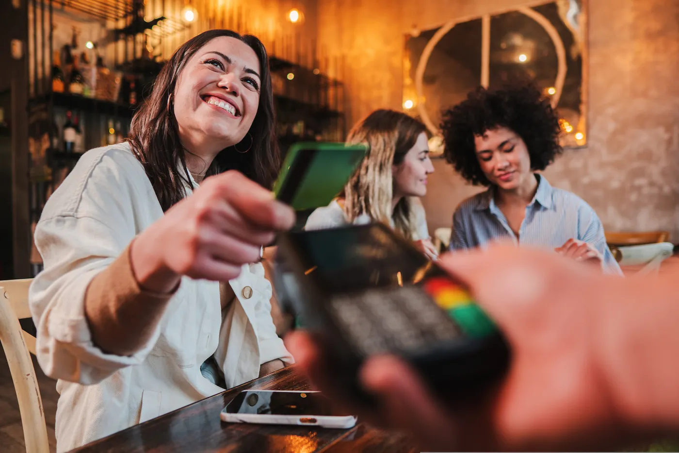 Happy young woman paying bill with a contactless debit card in a restaurant.