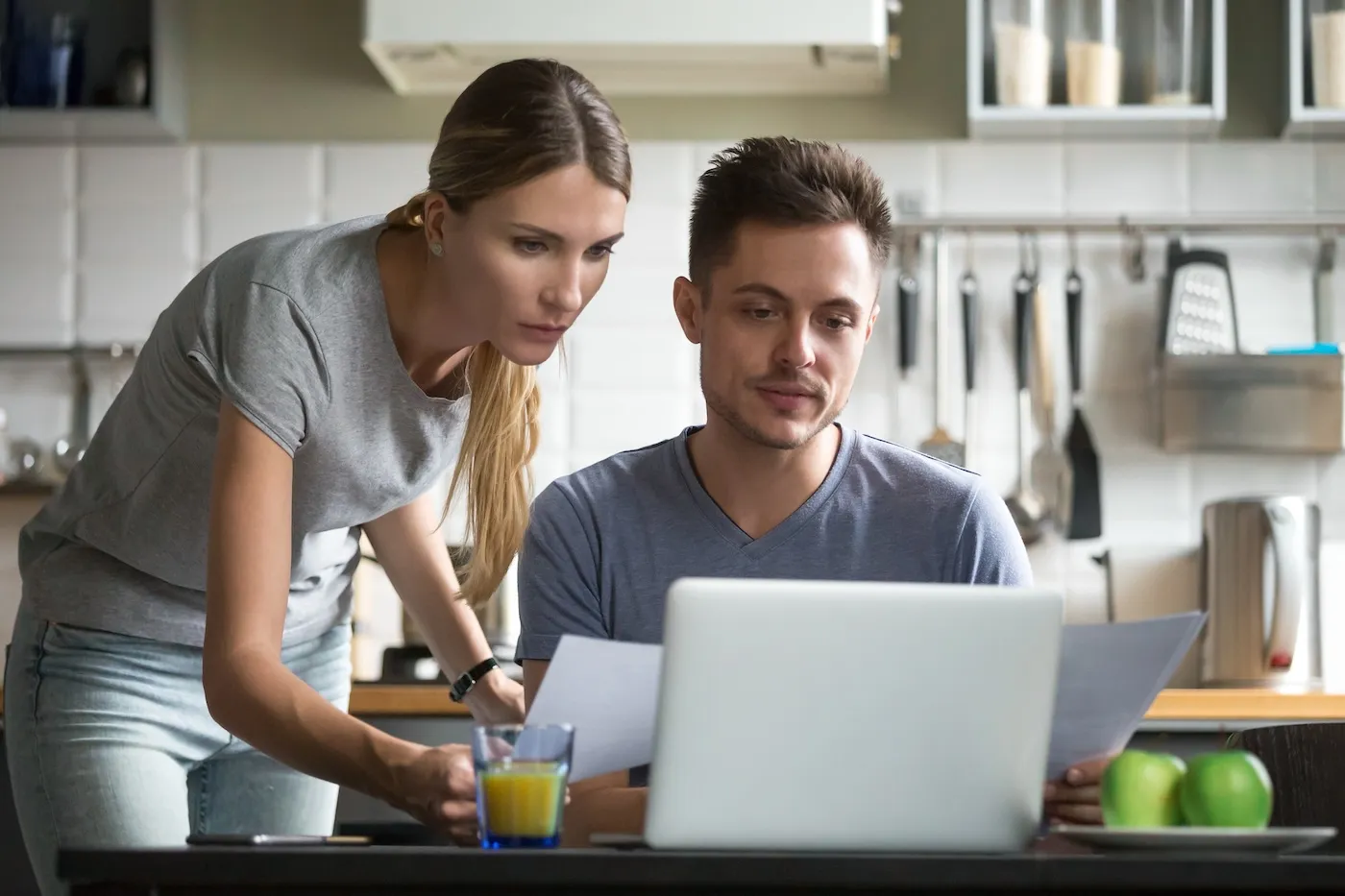 Serious young couple looking at online loan application form on a laptop in their kitchen.