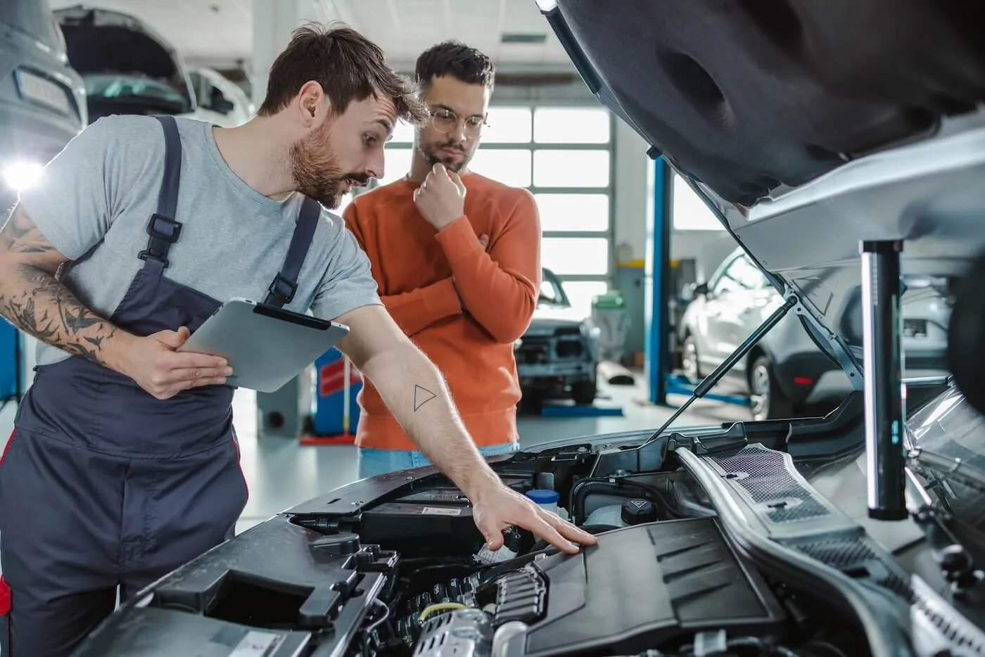 A mechanic at the car workshop is explaining the issue under the hood to a customer