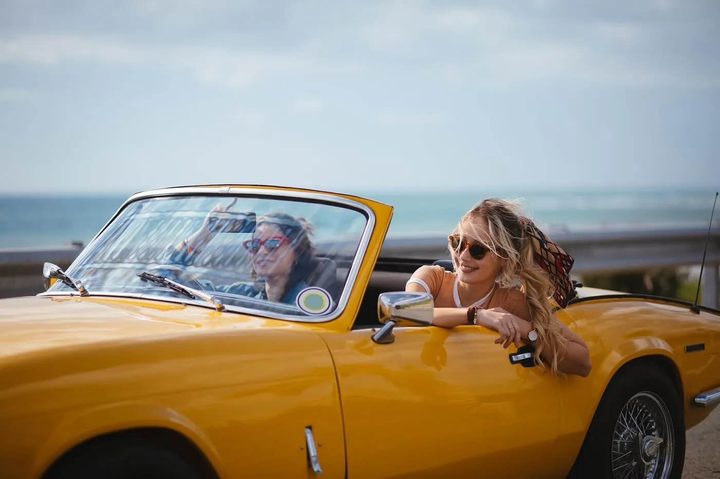 Two young women driving a yellow retro convertible on an ocean view road