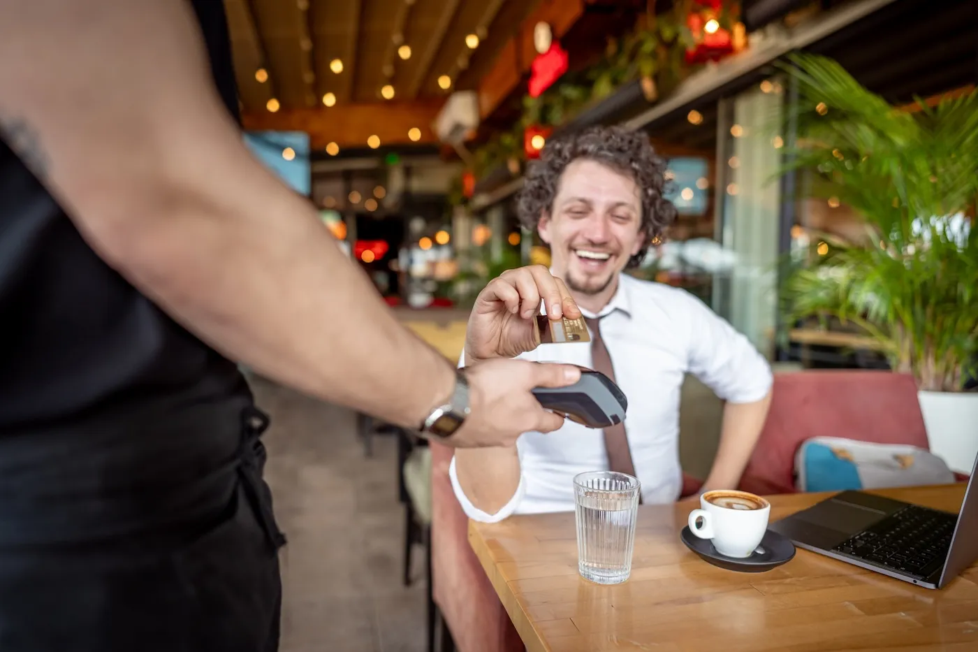 Elegant man dressed in a shirt and necktie using credit card on contactless payment terminal in cafe.