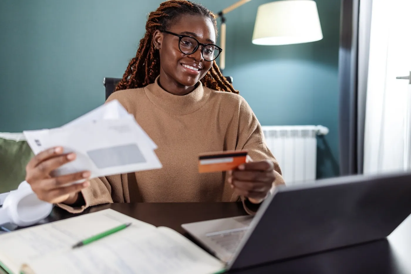 Young woman holding bills and a credit card. She is paying bills online on the laptop.