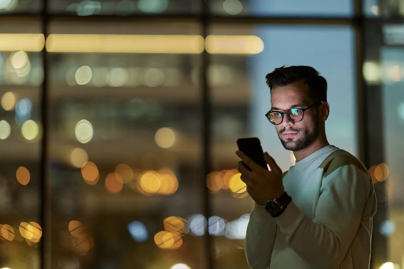 Young man using cell phone indoors at night.