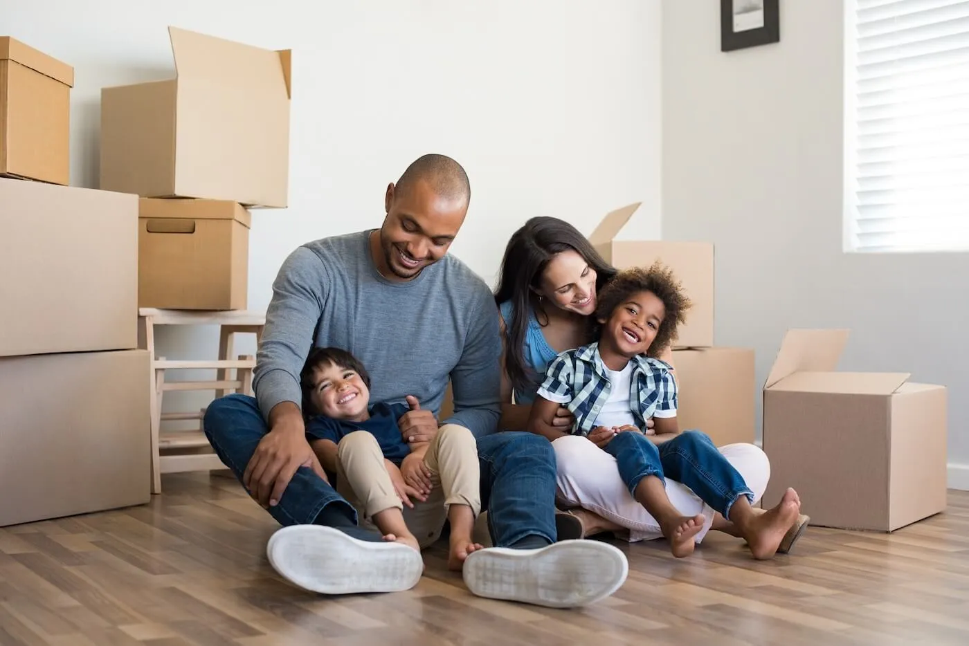 A happy family of four in their new house sitting on the floor surrounded by boxes