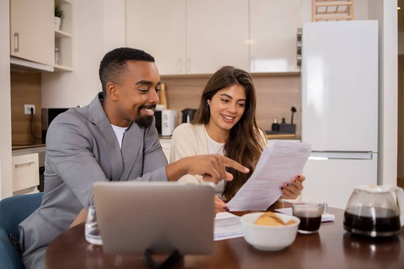 Happy couple planning their finances in the kitchen while using the laptop