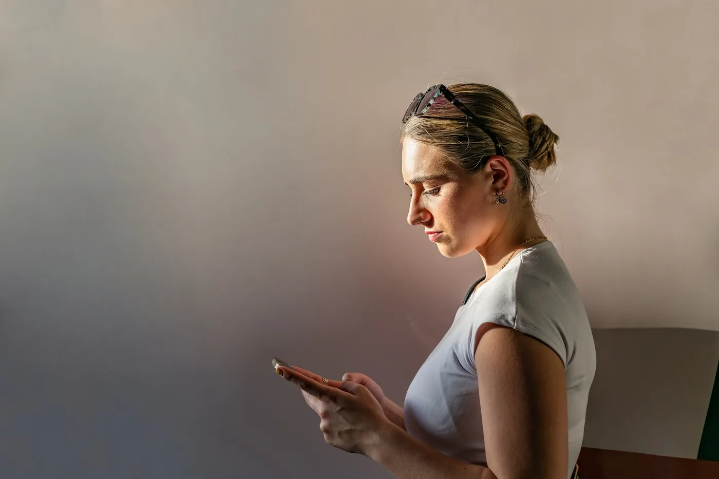 Profile view of a serious young woman looking at her mobile phone, lit by natural side light.