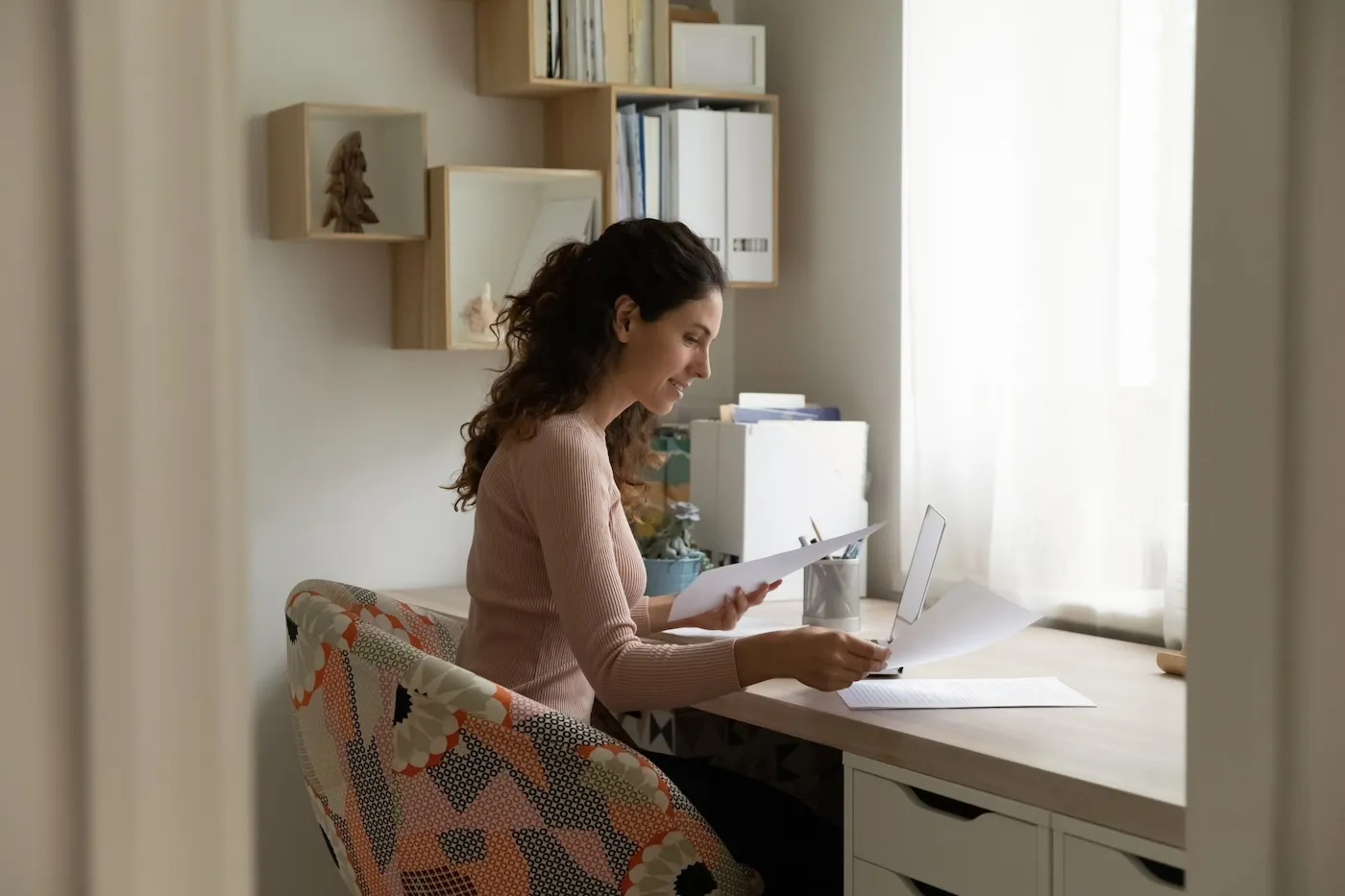 Smiling woman reading a gift letter for a mortgage while using her laptop in a home office