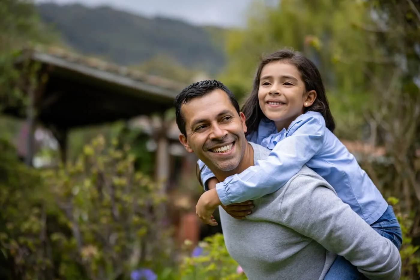 A smiling father is carrying a daughter on his back