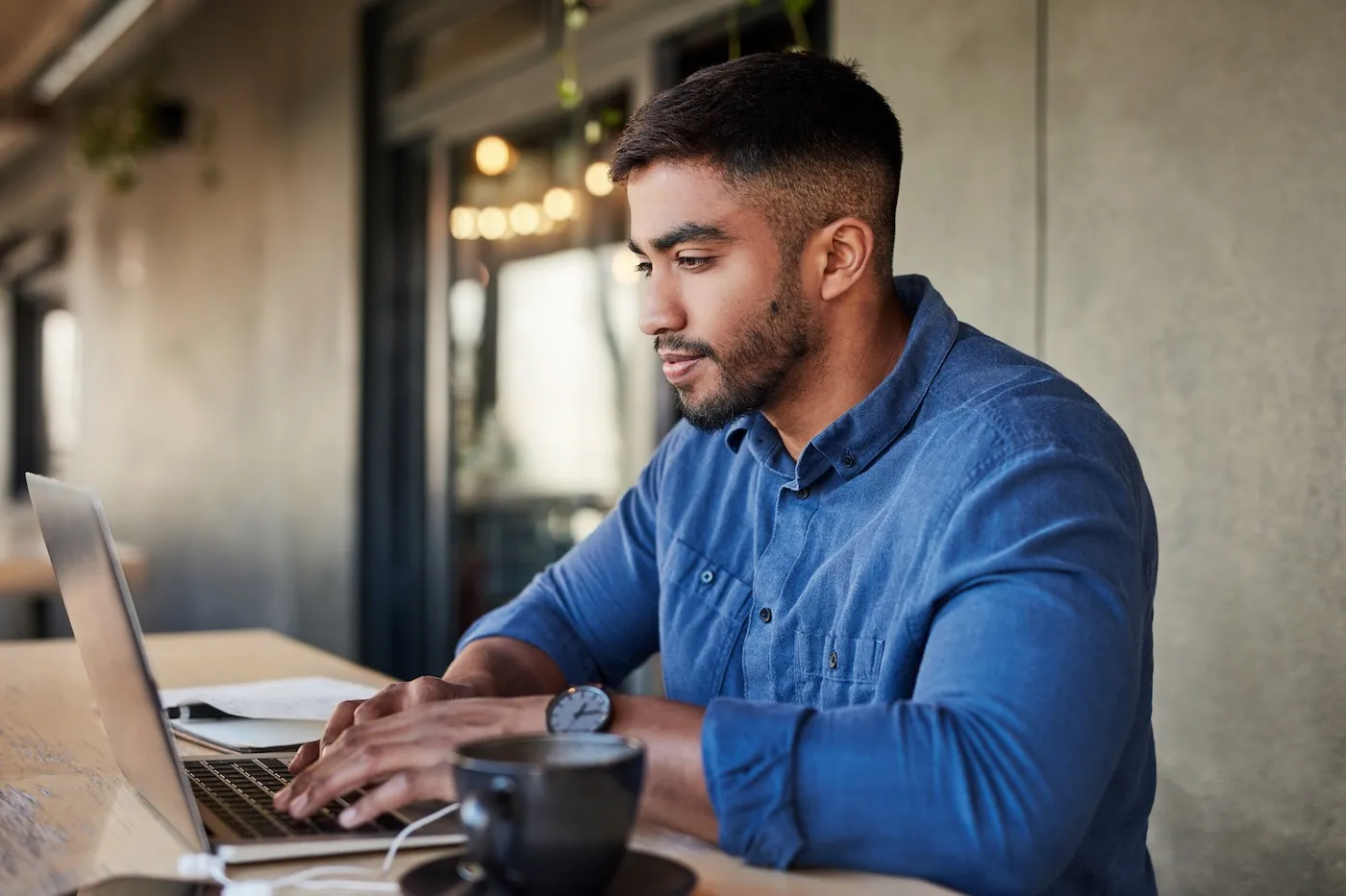 A man sitting at an outdoor table checking his investments on a laptop.