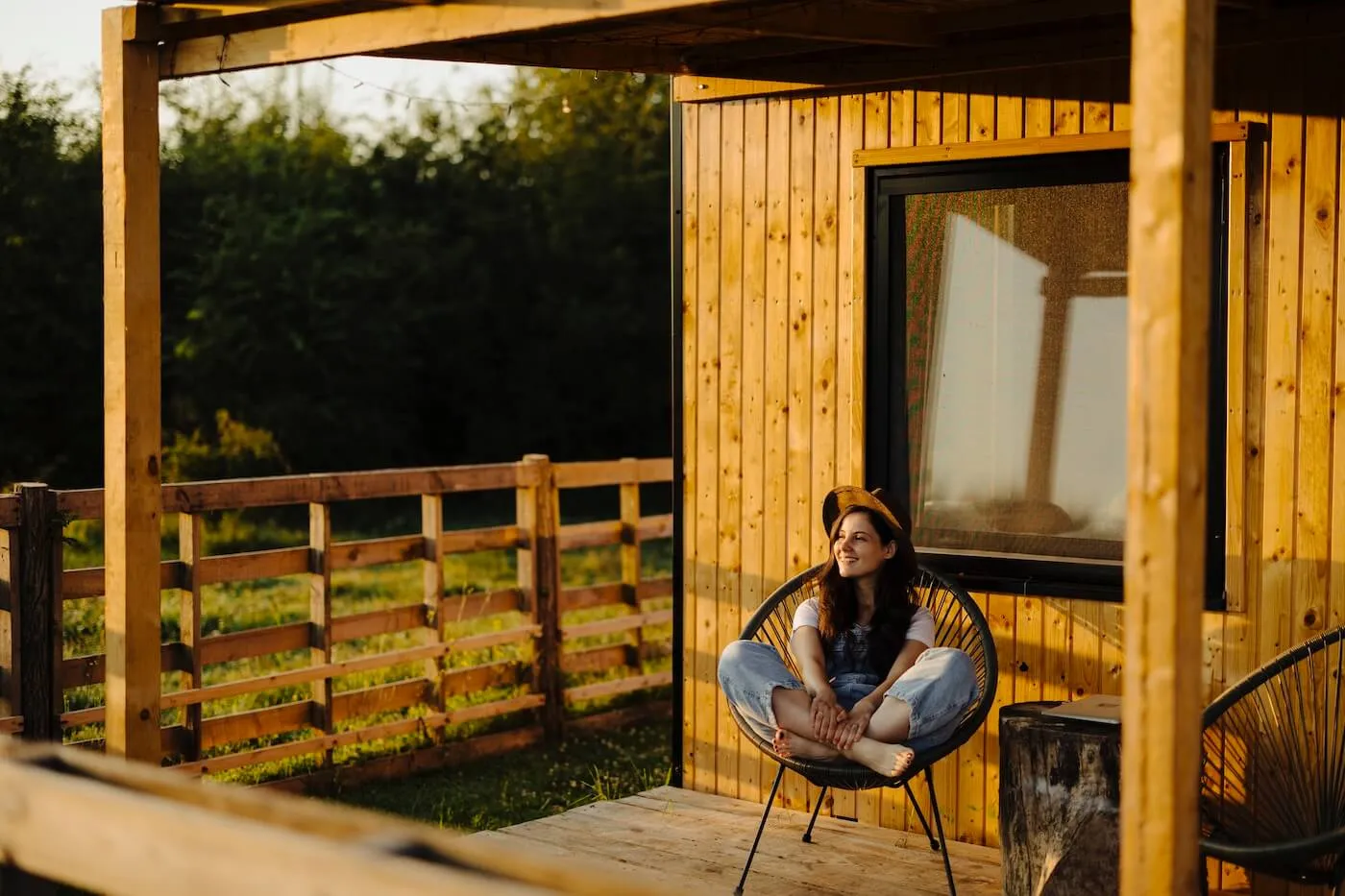 Smiling young woman sitting comfortably on the lounge chair on the manufactured house porch