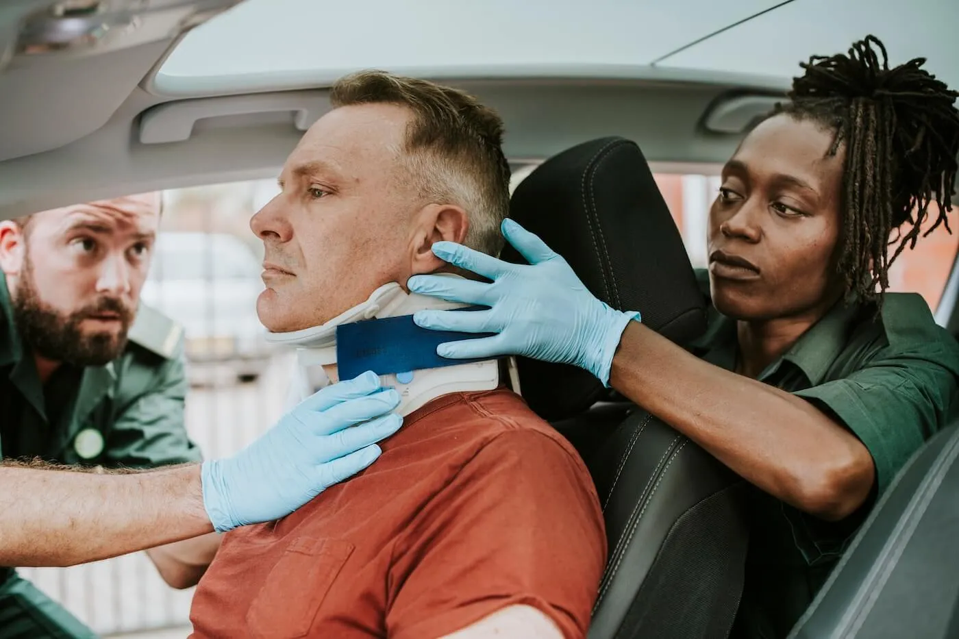 Two paramedics, male and female, are putting a neck brace on an injured man's neck in the car