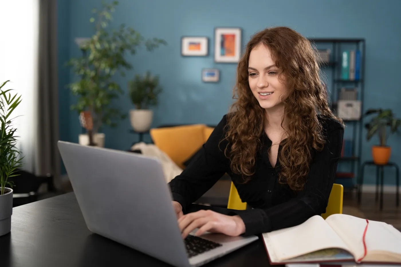 A woman using a laptop to check her credit score. She is sitting at a desk with a book next to her.