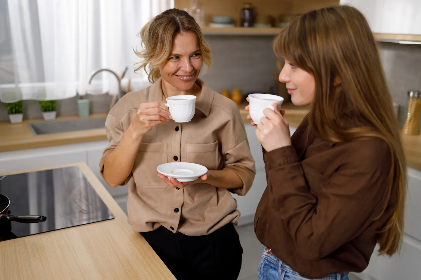 Happy mother enjoying in coffee with her teen daughter at the kitchen.