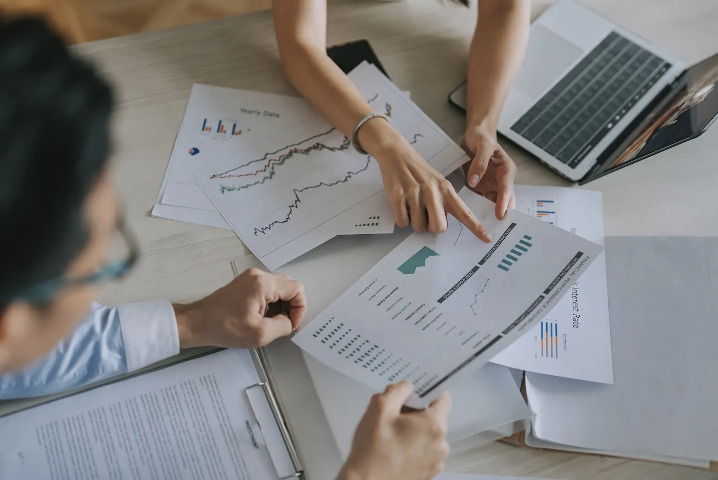 Two people reviewing investing documents on a table with a laptop nearby.