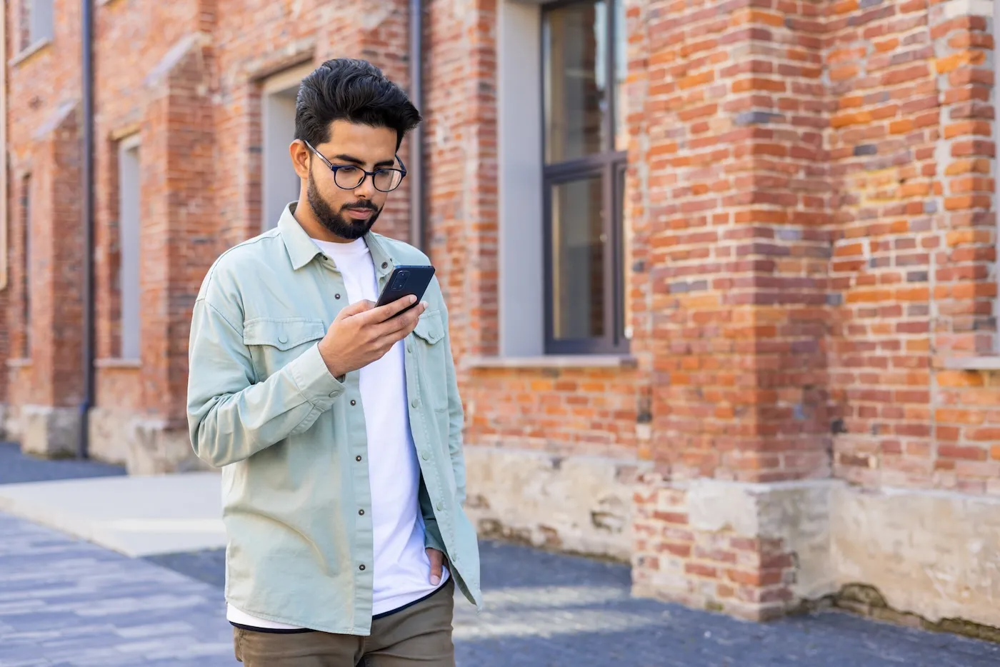 Serious thinking man with phone in hand walking outside office building.