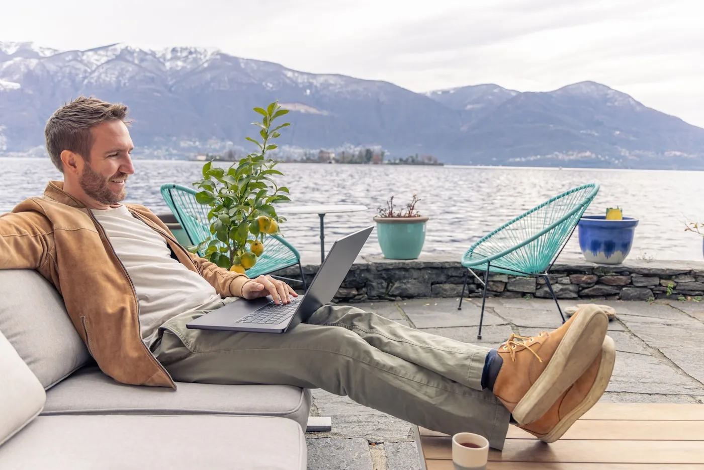 Man on his laptop on an outdoor patio by a lake.