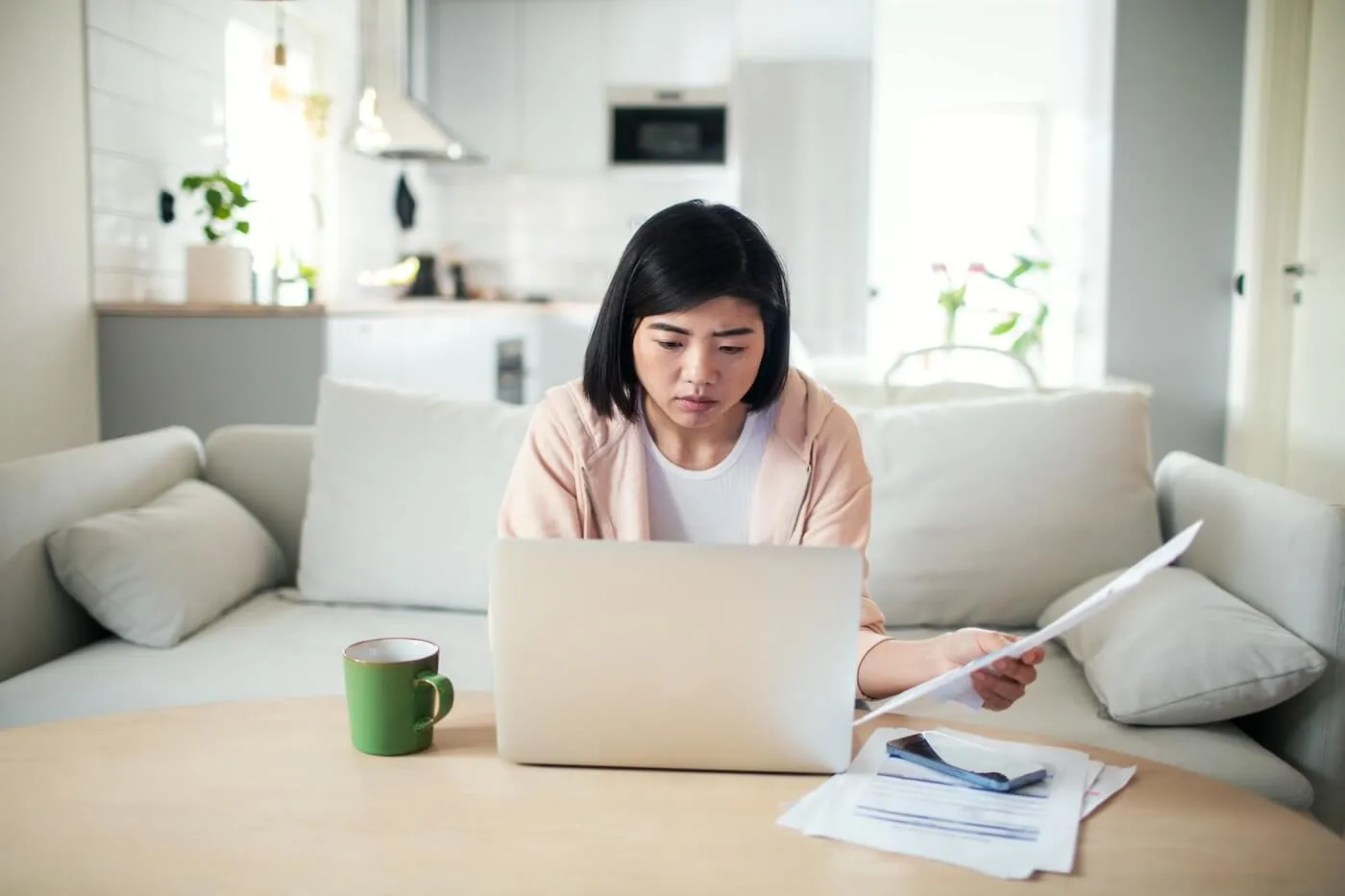 Concerned young woman holding a letter while using her laptop in the living room