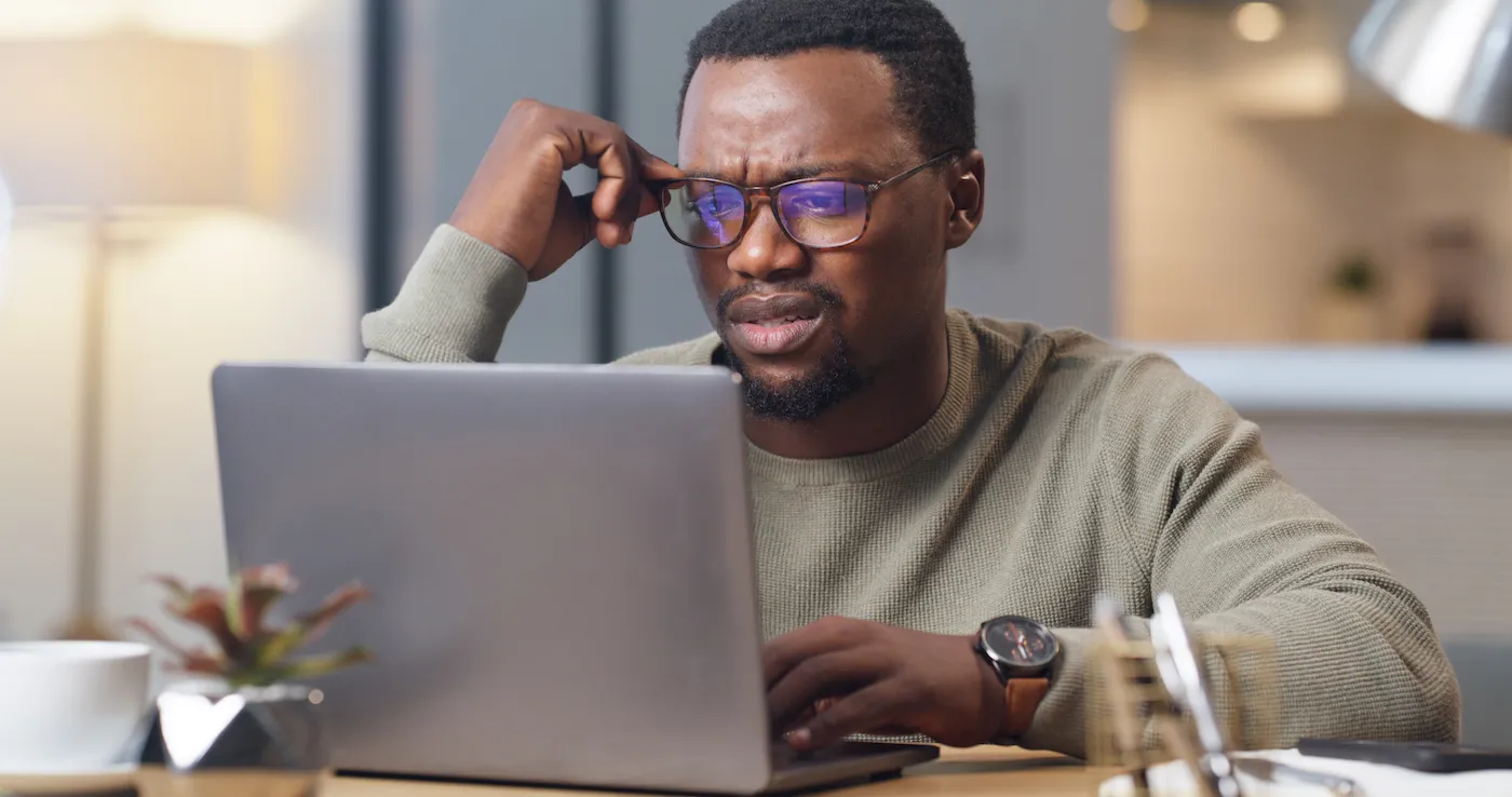 A man on a laptop in home office, reading his denied homeowners insurance claim.