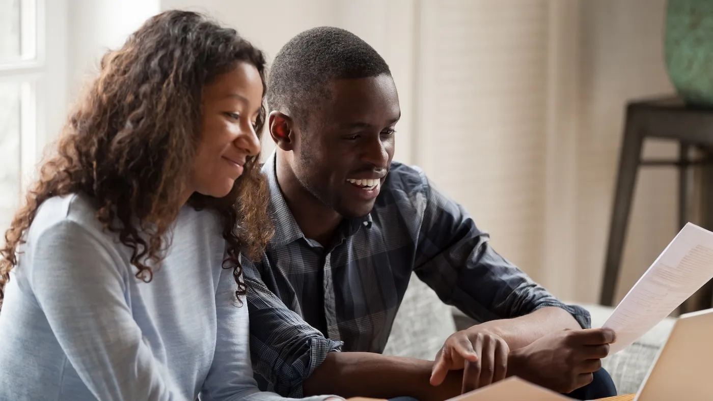 Happy couple holding up documents, deciding what to do with their tax refunds.