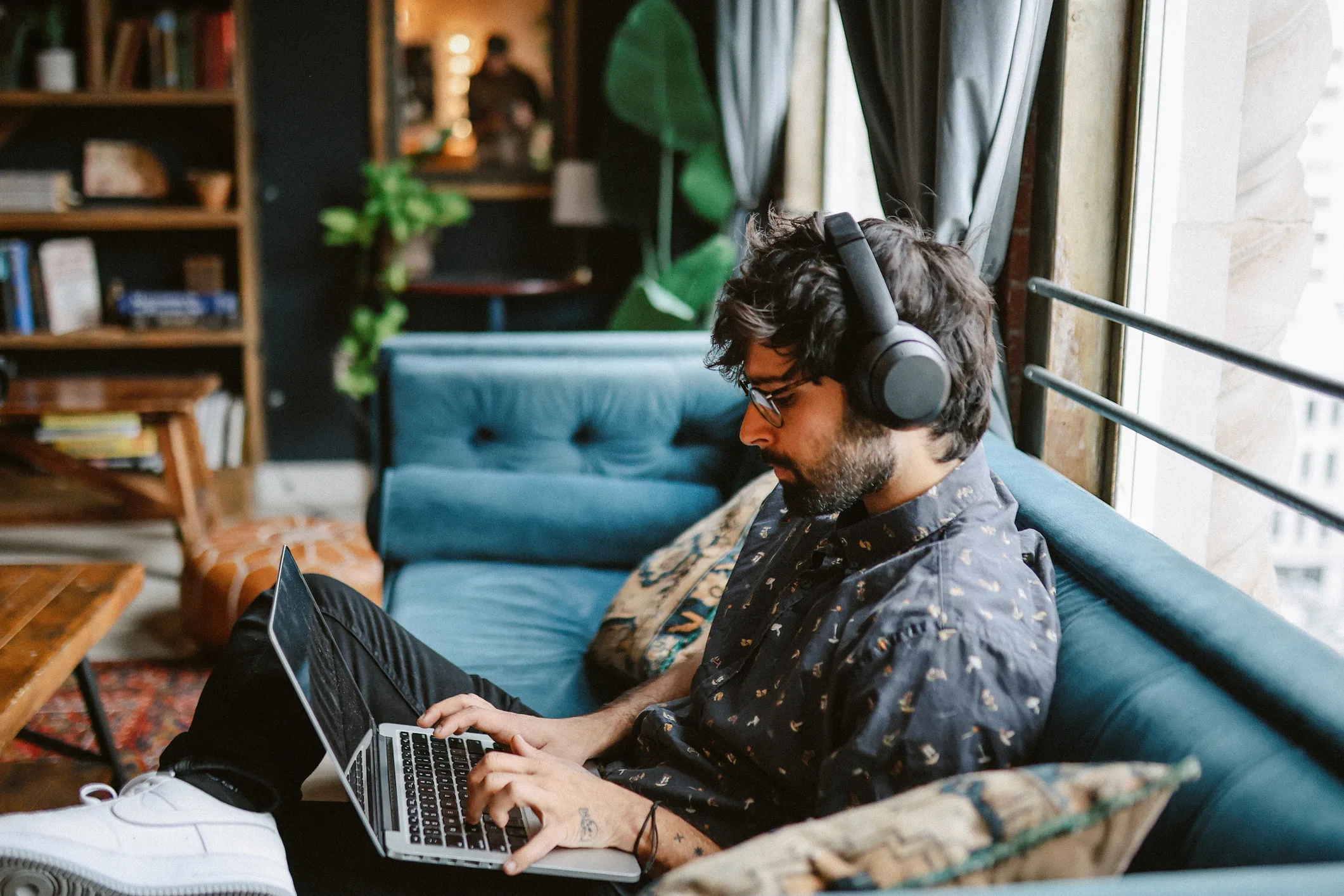 Young man reviewing credit report from home, sitting on a couch wearing headphones and using a laptop.