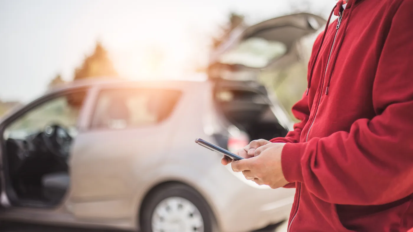 Man texting in front of car