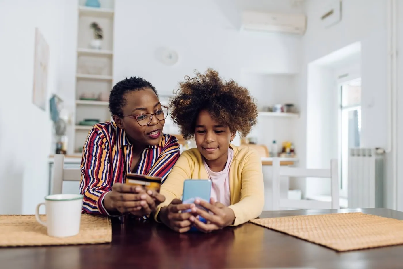 A woman with a young teenage kid making a payment via credit card and smartphone at home