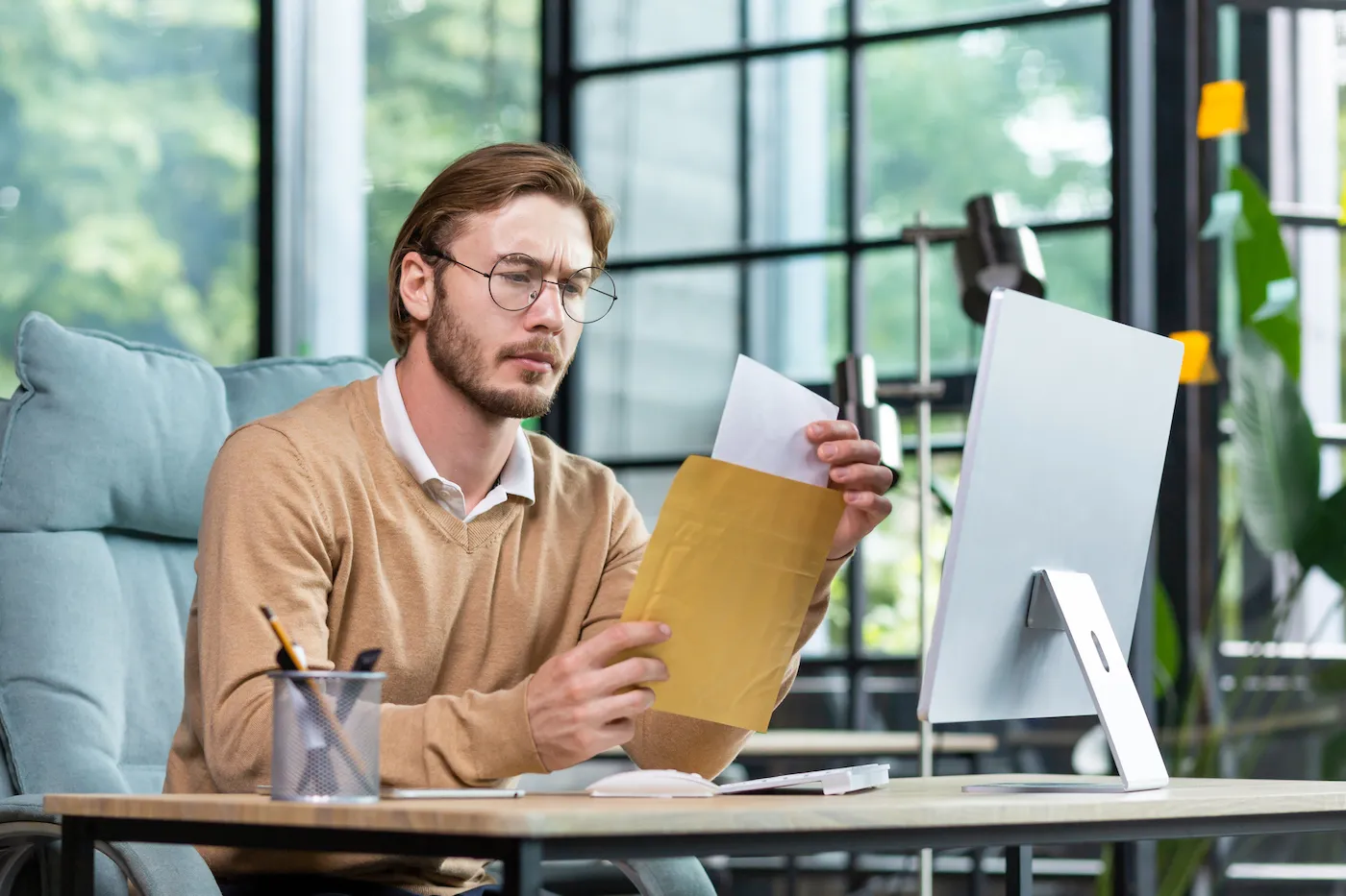 A young worried man sits at the desk in the office and reading a paper with his minimum payment.