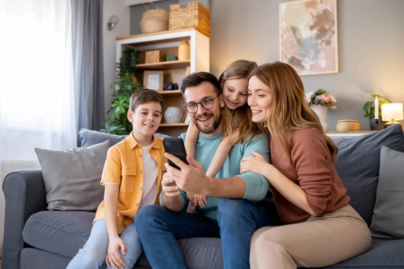 A happy family of four sitting on the couch and checking their savings account via smartphone