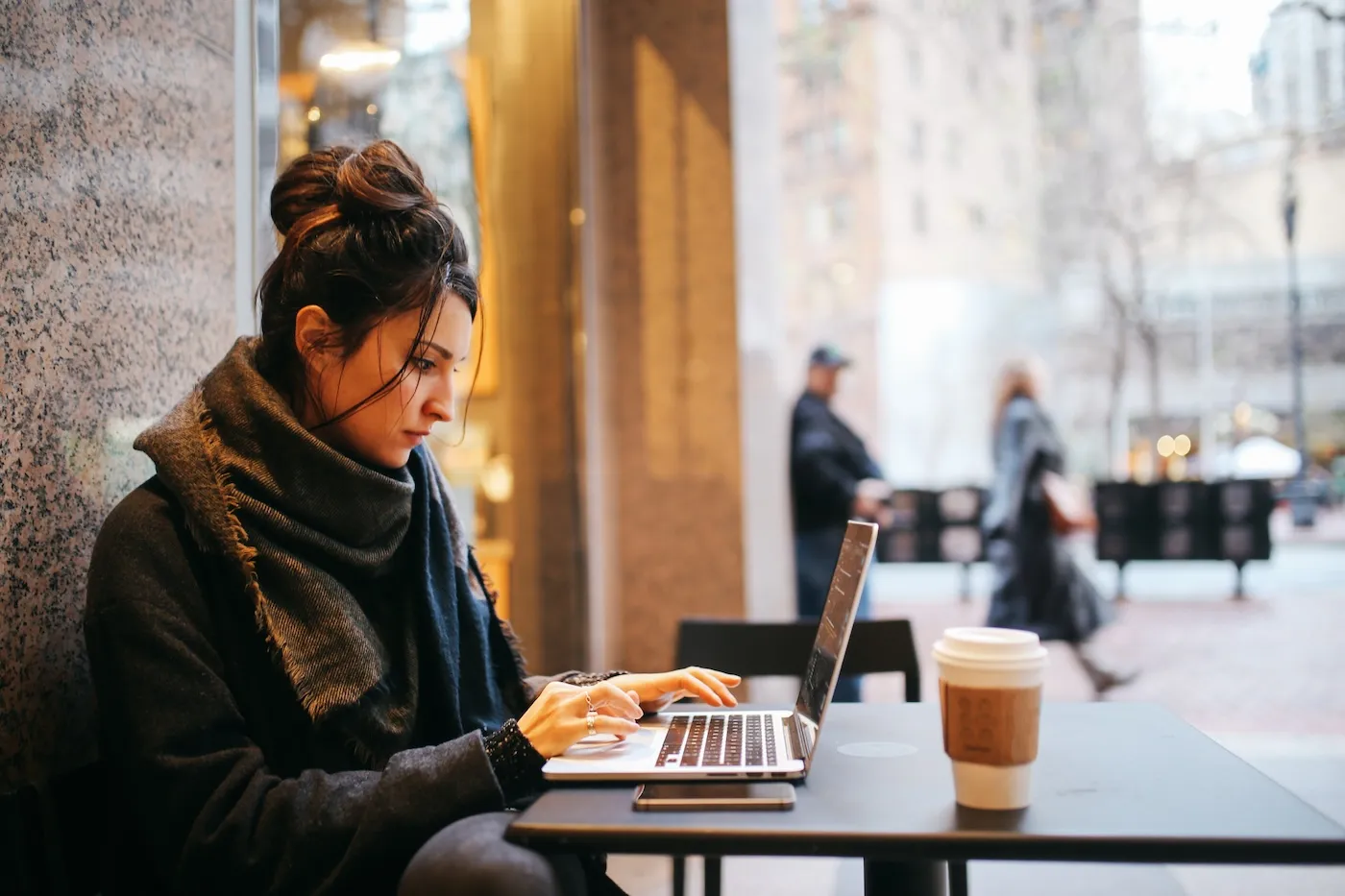 Young woman sitting outdoors in front of the cafe, finishing her work on the laptop, in San Francisco, California.