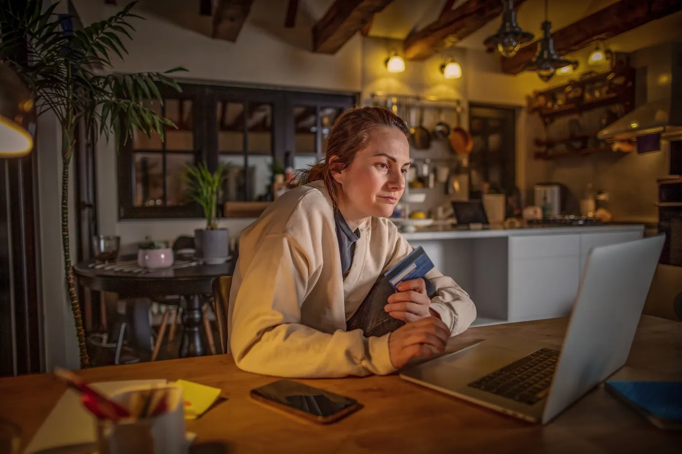 Photo of young woman preparing for a credit check, on her laptop in the kitchen late at night.