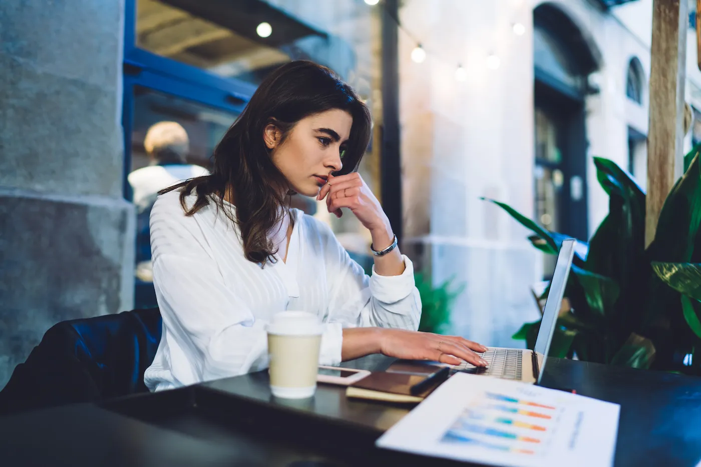 Side view of woman checking bank account on her laptop from an outdoor cafe table.