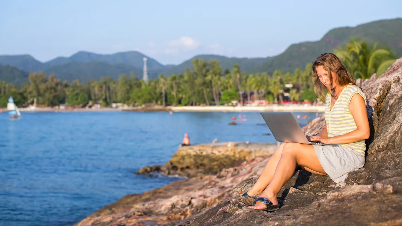 Girl checking credit score with laptop sitting at sea coast.