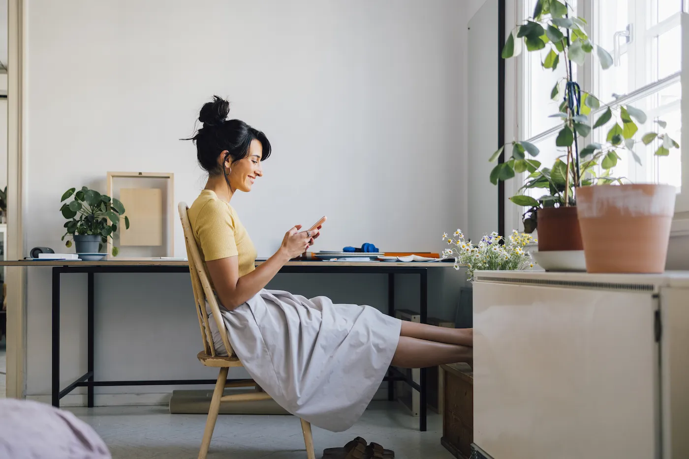 A woman sitting at her desk checking her savings account on her phone