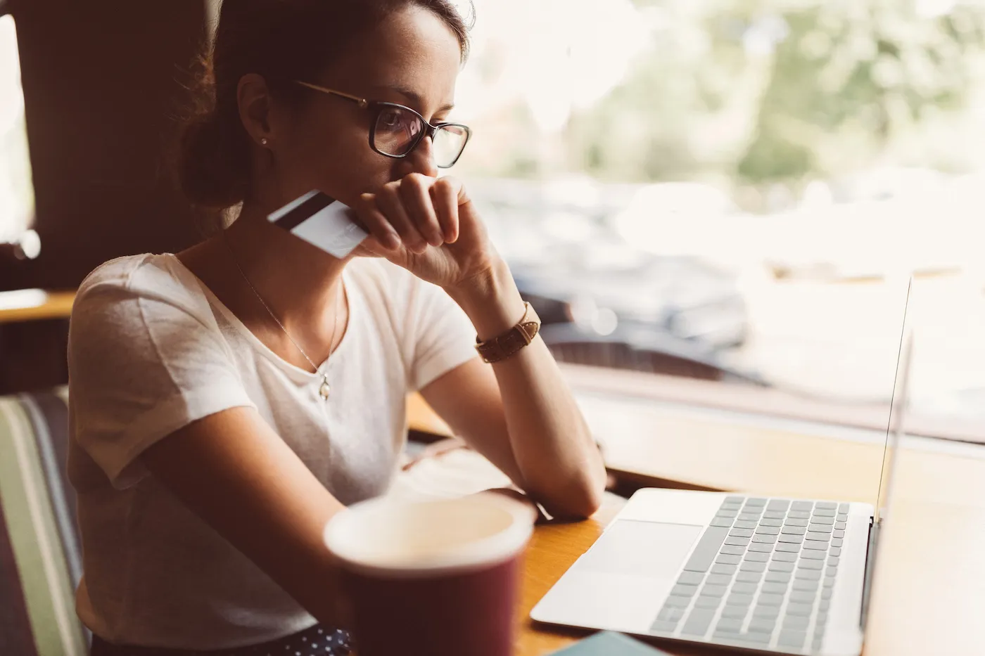 Concerned woman holding a credit card and looking at laptop worries about credit card fraud