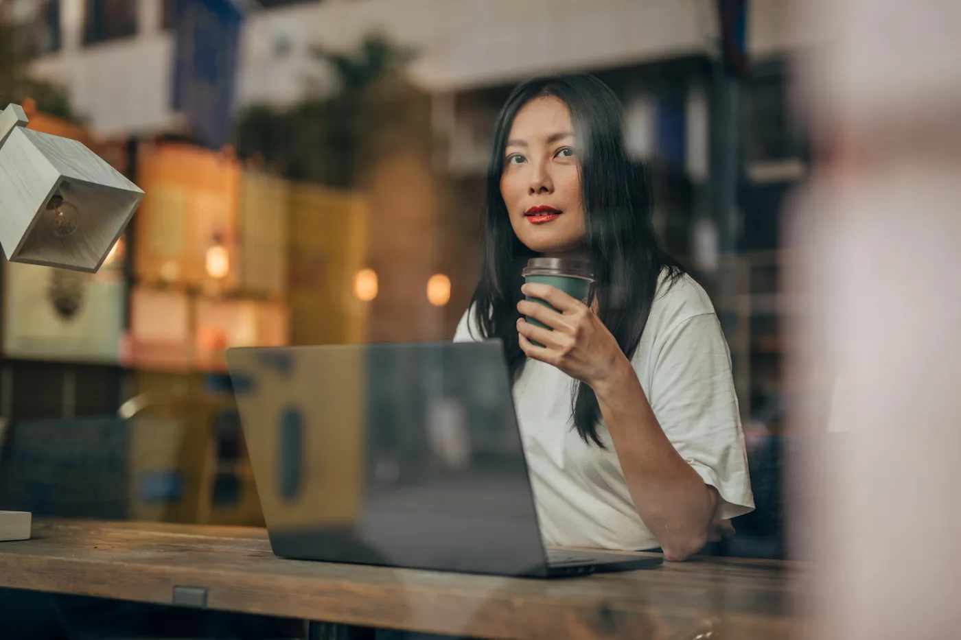 Young woman drinking coffee at the cafe and working on laptop, contemplating what types of debt can go to collections.