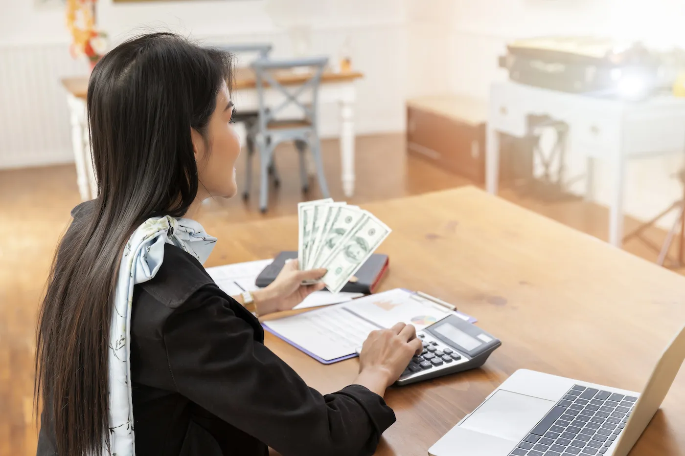 Woman holding money using calculator at table.