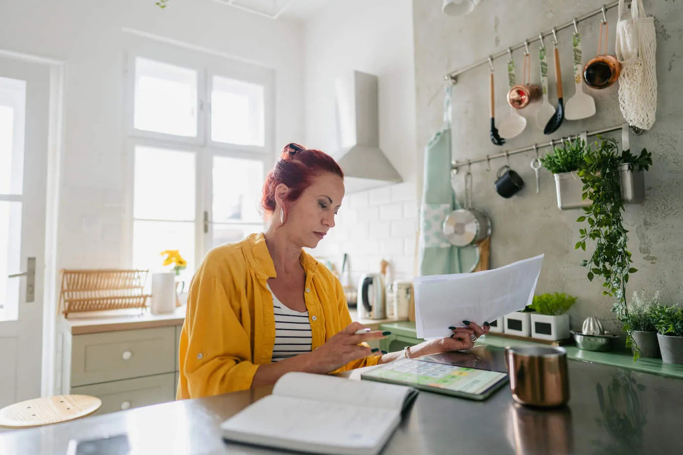 Woman in yellow jacket reseting her finances while seated at the kitchen island.