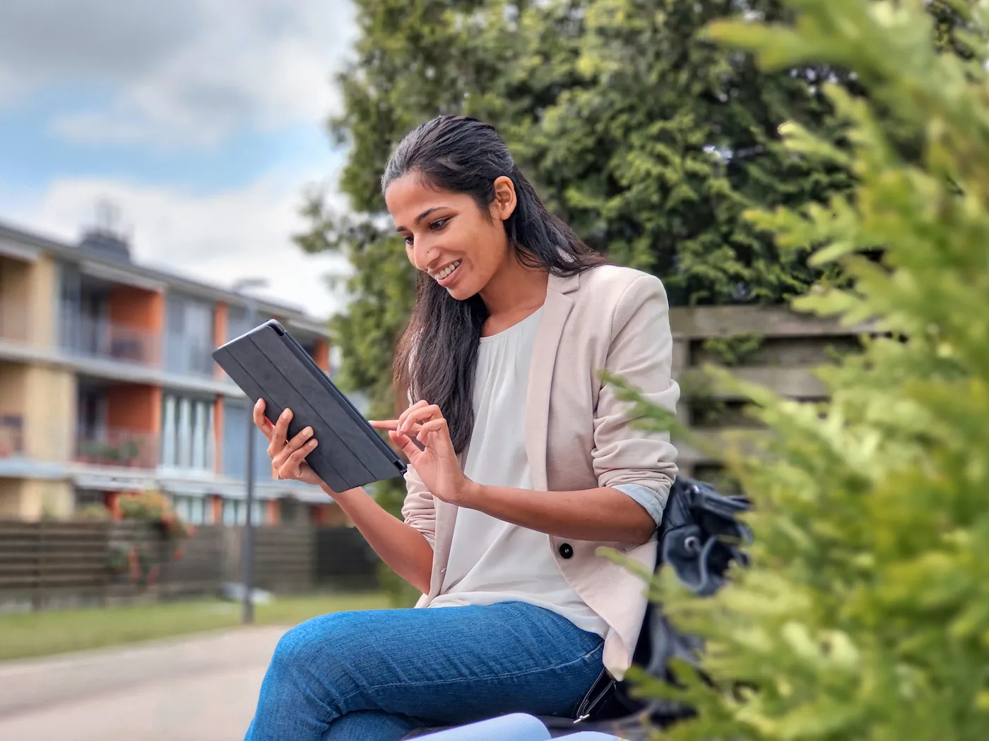 A woman working outdoors with a digital tablet, researching fees for high yield savings accounts.