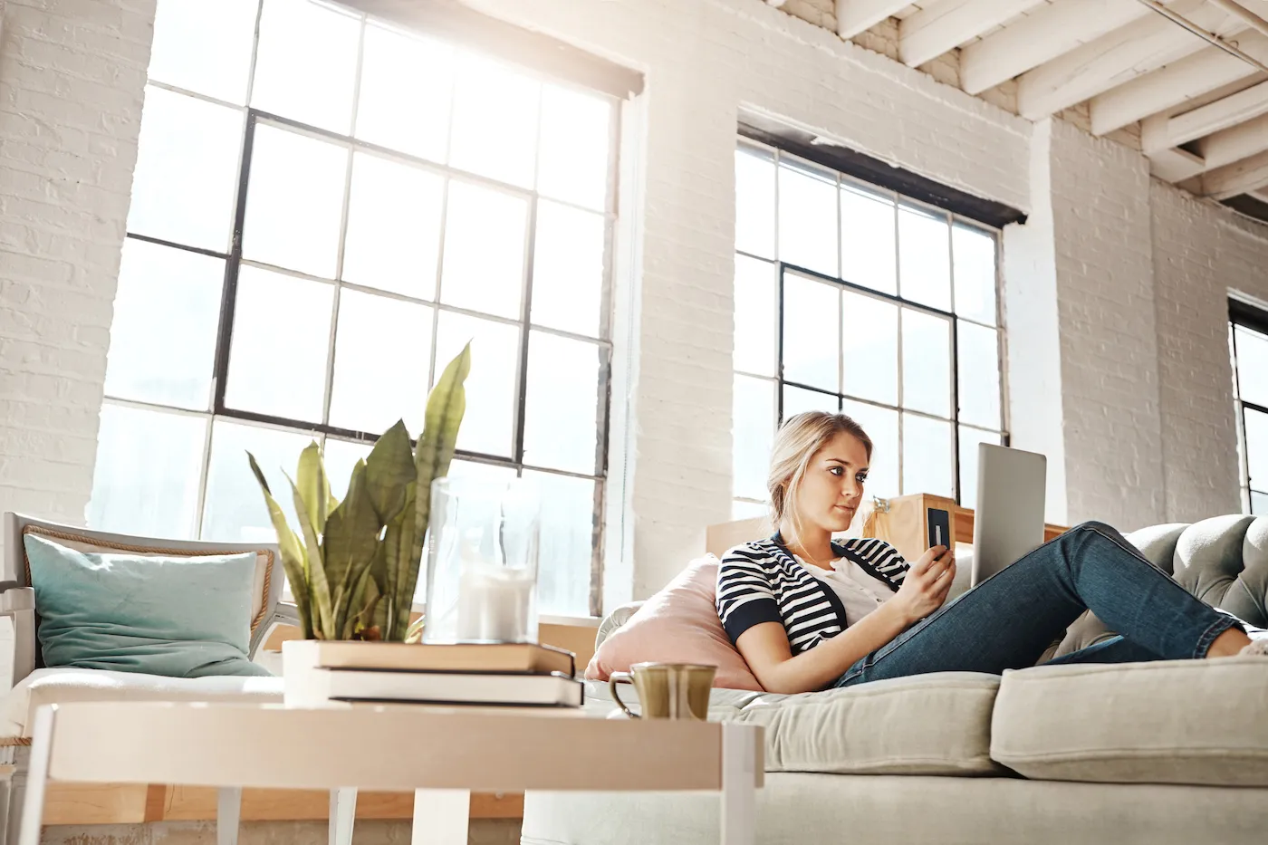 Shot of a young woman relaxing on the sofa and using a credit card with a laptop