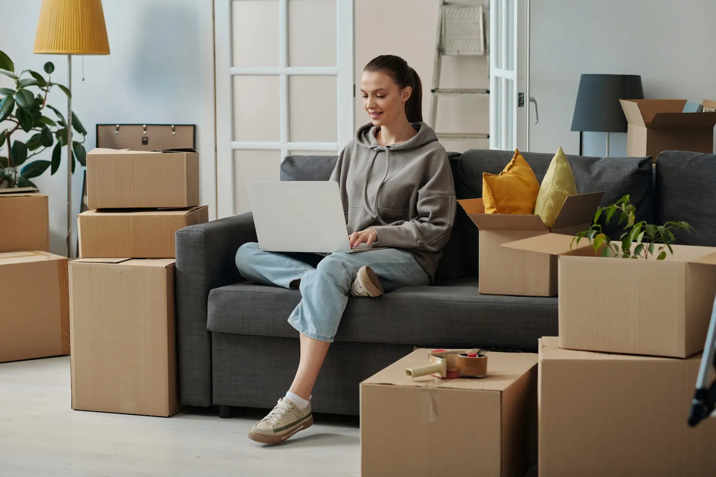 Girl sitting on sofa and using laptop to research mortgages and personal loans during her moving in new house