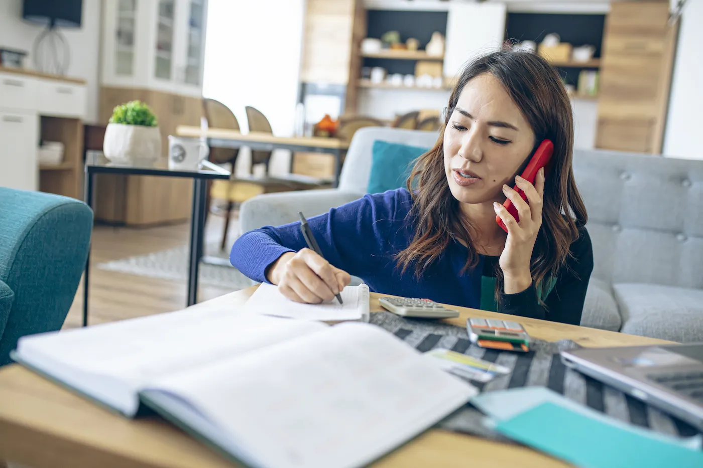 Woman sitting on the floor on the phone, writing out her debt management plan on papers on the coffee table.