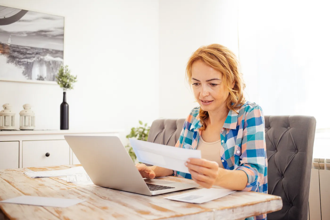 A woman sitting at her desk with papers and a laptop, shopping for loan rates