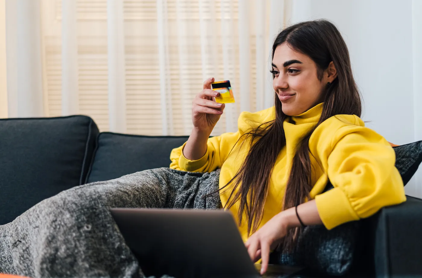 Smiling young woman, covered in her blanket, checking out her new rewards credit card.