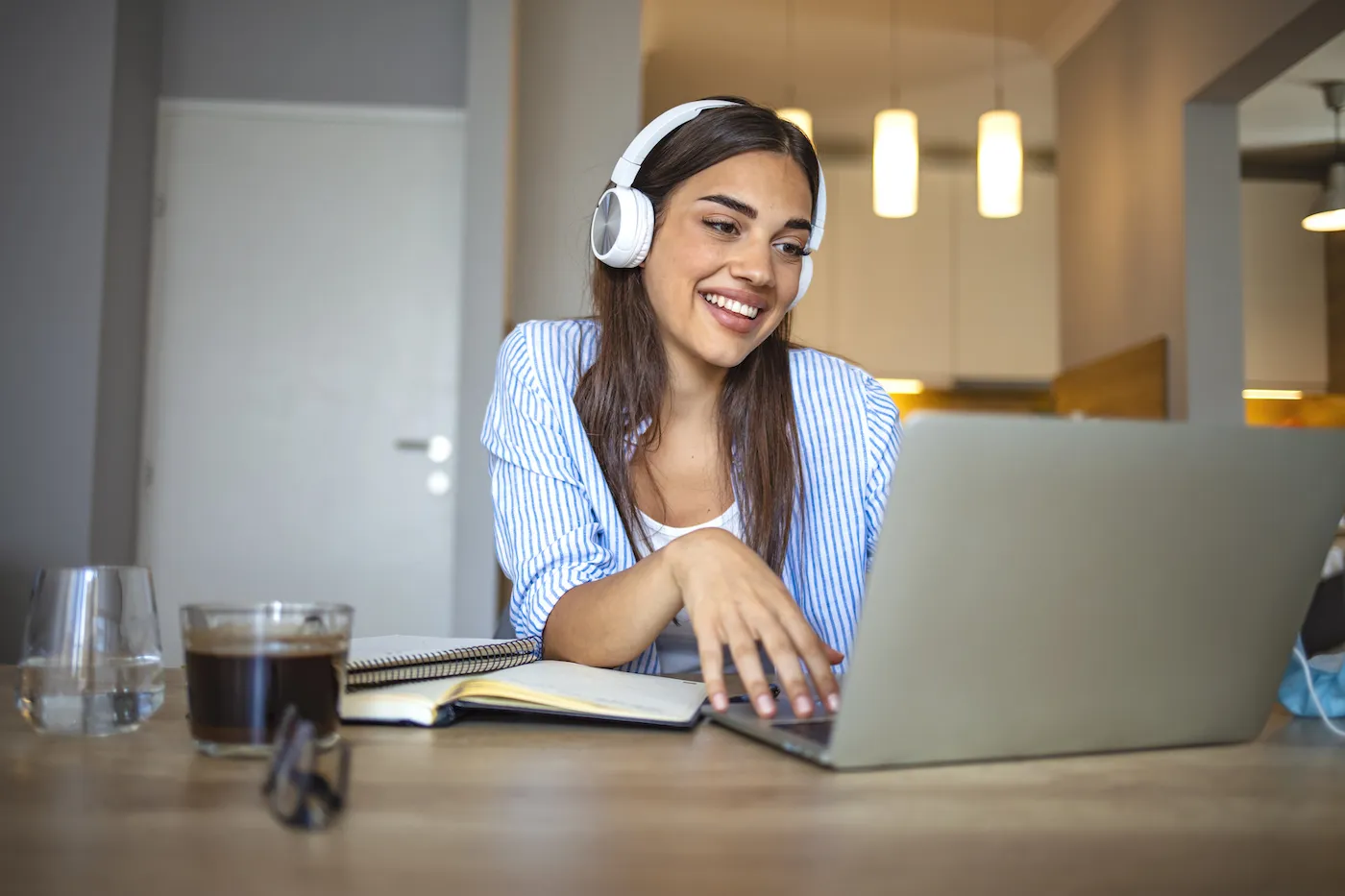 A woman wearing wireless headphones and talking to strangers online using her laptop.