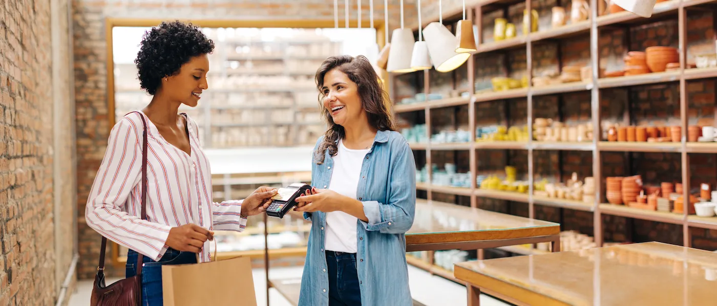 A woman using her credit card in a small ceramics shop with the store clerk holding the point-of-sale card scanner.