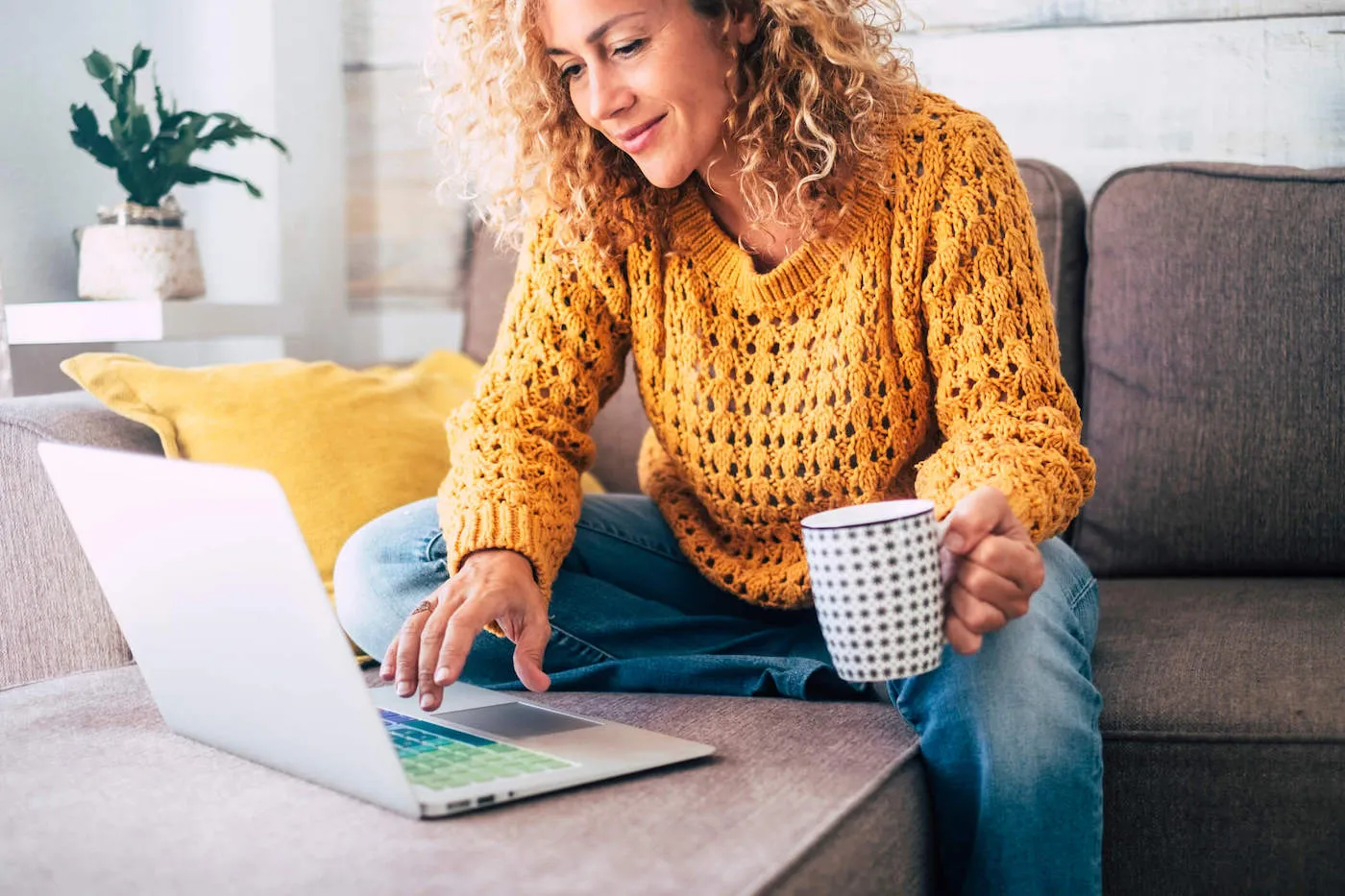 Woman with curly hair seated on sofa working on notebook at home.